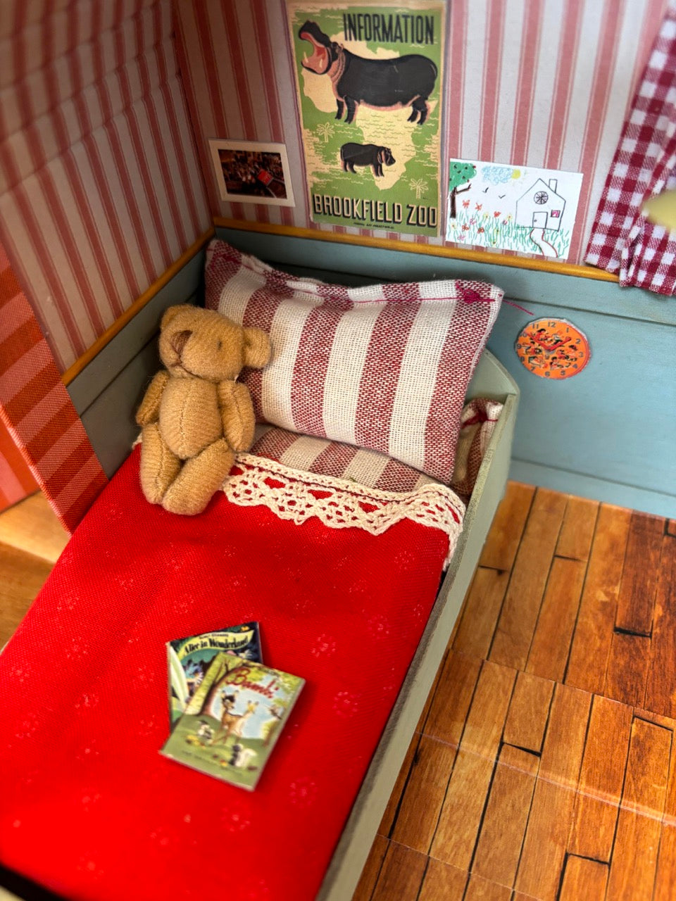 Detail van Sam & Julia Muizenhuis slaapkamer met bed, rood dekentje, kussen en wanddecoratie in poppenhuis koffertje