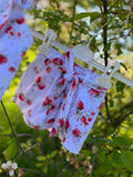 Witte meisjes short met aardbeienprint en strikdetail, gefotografeerd buiten tussen groene bladeren.