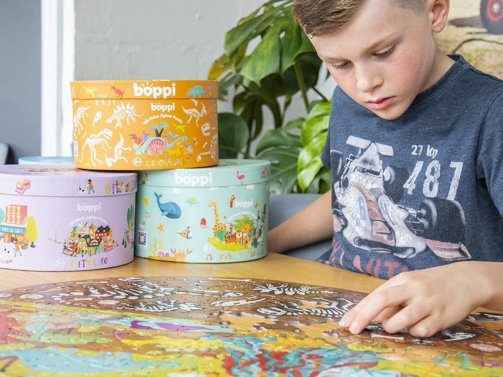 Kind dat een ronde dinosaurus puzzel legt aan tafel, met meerdere ronde puzzeldozen op de achtergrond.