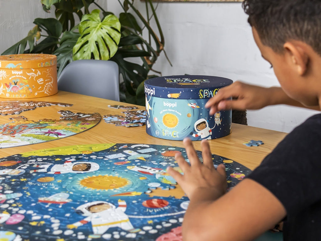Ronde kinderpuzzel met ruimte-thema op tafel, puzzelstukken en doos zichtbaar terwijl een kind de puzzel legt.