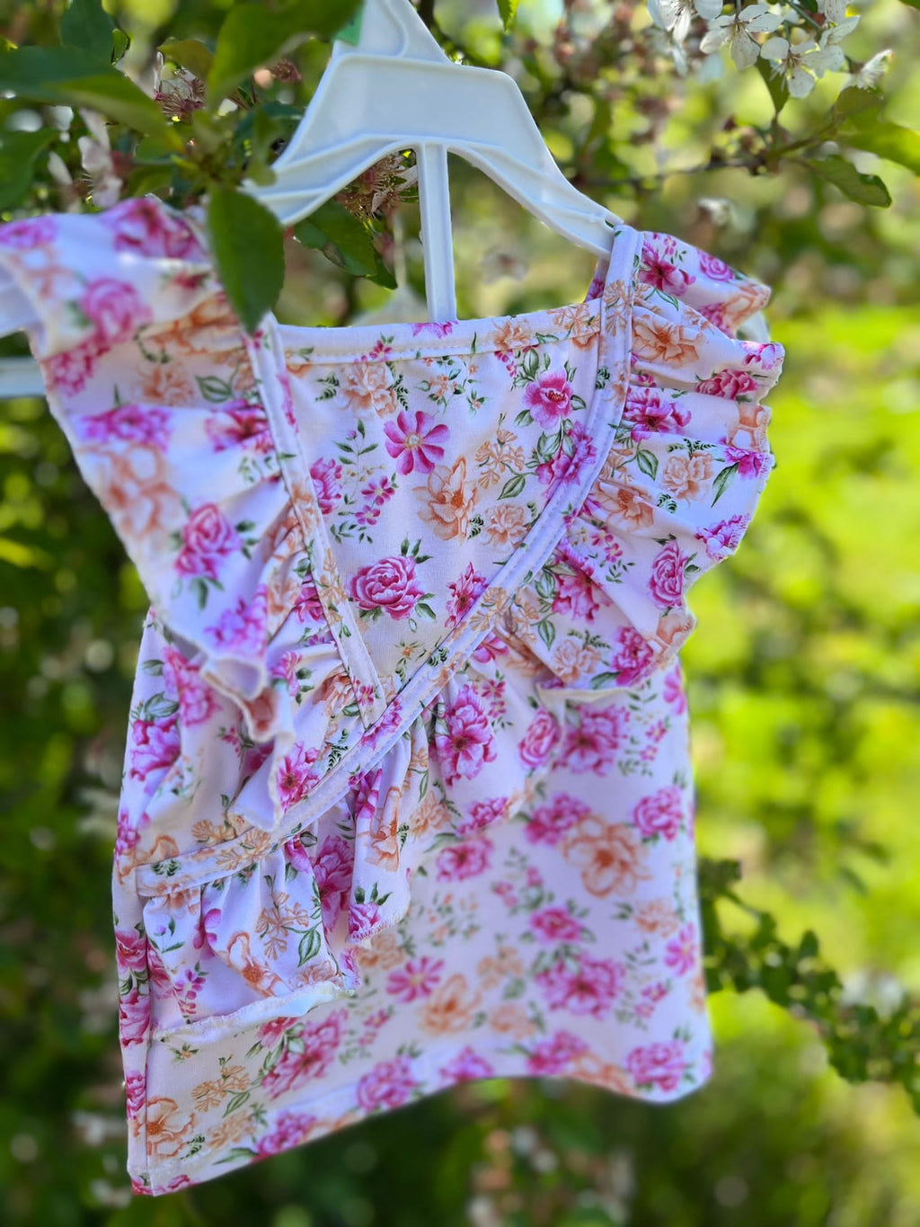 Meisjes zomerse top met bloemenprint en ruches, gefotografeerd buiten tussen groene bladeren.