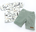 Jongens zomerset met T-shirt met vliegtuigprint en groene short, gefotografeerd op witte achtergrond.