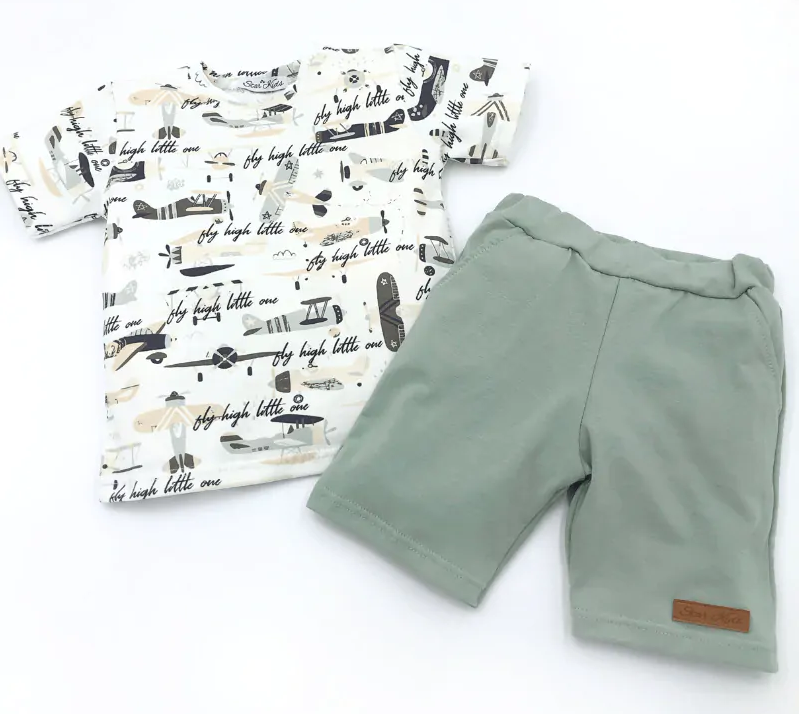 Jongens zomerset met T-shirt met vliegtuigprint en groene short, gefotografeerd op witte achtergrond.