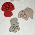 Drie siliconen bijtringen met pop-it in vormen van paddenstoel, olifant en dinosaurus
