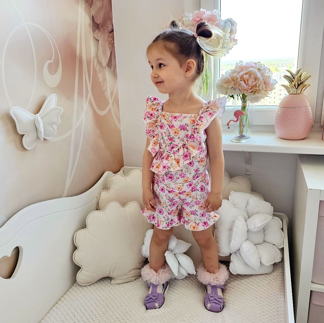 Meisjes zomerse T-shirt met bloemenprint en ruches, gedragen door een kind in een lichte kinderkamer.