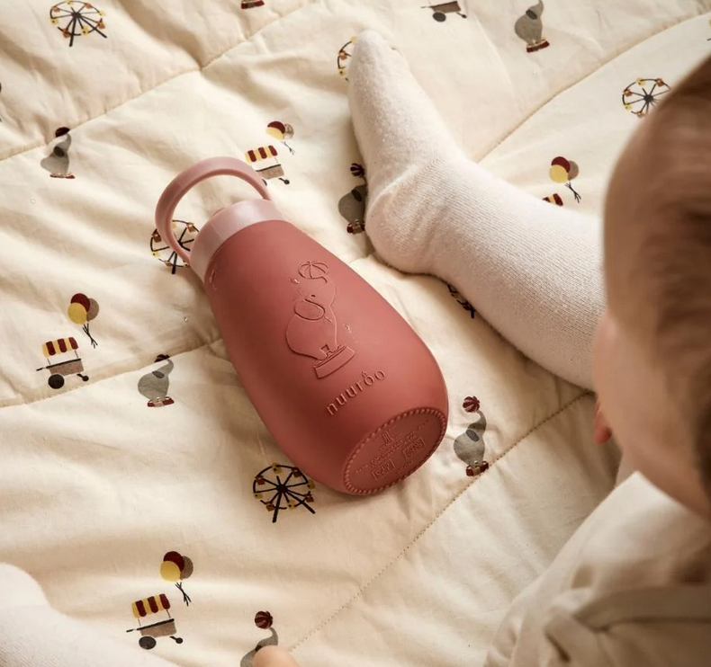 Roze baby drinkfles liggend op speelmat naast kind